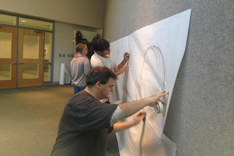 Art teacher Matt Ravenstahl, AFAFA co-founder Ainsley Eakins, and senior Kaitlyn Prisciandaro draw on paper in the art gallery across from the main office as part of the Big Draw campaign. Students are encouraged to add to the wall throughout the month of October. 