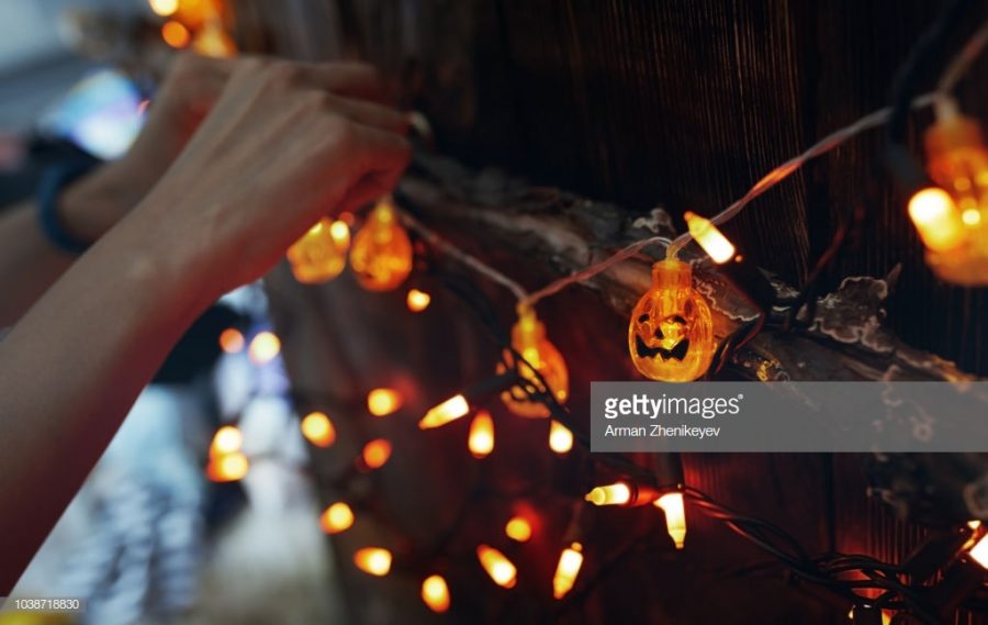 Woman hanging decorative eletric light with pumpkins. Halloween theme. Photo by Arman Zhenikeyev through Getty Images