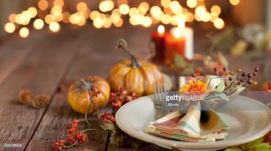 Autumn Thanksgiving dining table place setting on an old rustic wood table with candles and defocused Christmas lights